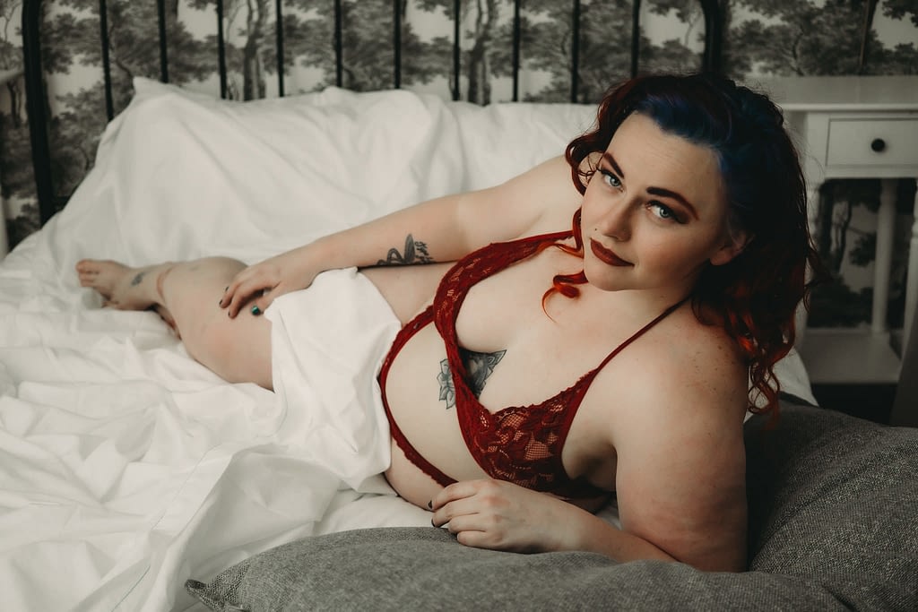 Women posing on bed wearing red lingerie keeping elbow on grey pillow.  Photo by Embodied Art Boudoir. Boudoir photography, denver boudoir photographer, colorado boudoir, photoshoot, golden colorado, sexy photoshoot, modest boudoir, intimate portraits, sensual photos, modest boudoir, risque, scandalous, scripts, funny