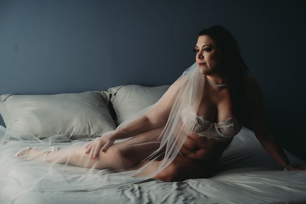 Women sitting in dark room on bed wearing white lingerie, net veil and white choker.  Photo by Embodied Art Boudoir. Modest photography, modest boudoir, modest photoshoot outfit, modest outfit ideas, boudoir photography, boudoir photoshoot, boudoir session, covered up, Colorado photographer, Denver boudoir photographer, Colorado boudoir photography, studio photography, body positivity, body positive photography
