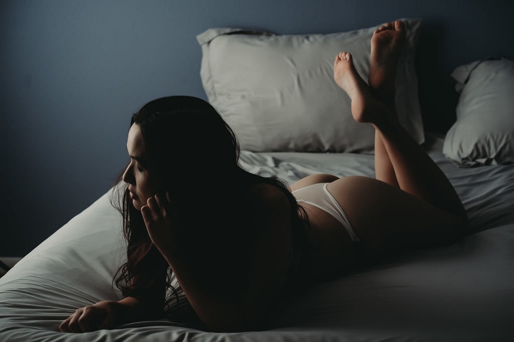 Women with closed eyes laying on the bed with crossed legs and closed eyes in dim light. Photo by Embodied Art Boudoir. Invest in yourself, investment, self love, self care, body appreciation, growth, growth mindset, learning, massage, rest, volunteer, forgiveness, nvc, nonviolent communication, declutter, self care tips