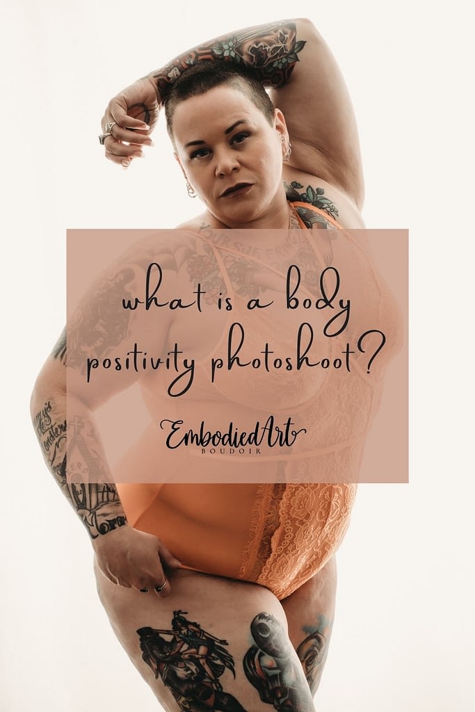 Shaved head plus size woman glowing in front of a white wall, covered in tattoos, wearing a bright orange sheer bodysuit, and staring intensely into the camera. Photo by Embodied Art Boudoir. Body positive, body positive photography, fat positive, fat positive art, fat positive photography, colorado boudoir, denver boudoir, boulder boudoir, body positive colorado, haes, plus size photography, plus size art, women, beautiful, body positive art, big body art, you are beautiful, inclusive photography, inclusive art, celebrate all bodies, diverse photography
