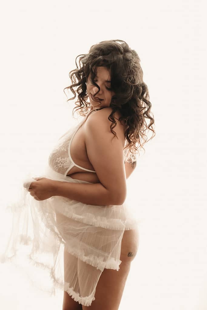 Woman with curly brown hair gracefully moving her white matching lingerie set and skirt.  Photo by Embodied Art Boudoir. Boudoir photography, boudoir photos, denver boudoir, colorado boudoir, denver boudoir photographer, pinup, pin up, pin-up, boudoir studio, boudoir session, sensual photography, fine art nude photography, fine art nudes, boudoir, boudoir history, photography history, 70s photography, 70s photoshoot