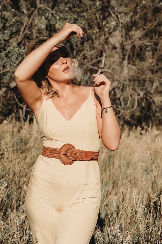 Blond woman standing in a grassy field smoking a cigarette wearing a beige jumpsuit with a brown statement belt. Photo by Embodied Art Boudoir. Modest boudoir photography, Modest Fashion, Modest Woman, Fashion Trends, Shy, classy photography, classic boudoir, classy boudoir, feminine photography, colorado boudoir, denver boudoir, boulder boudoir, colorado springs boudoir, boudoir ideas, boudoir poses, boudoir inspiration, photography inspiration, boudoir session, boudoir photos
