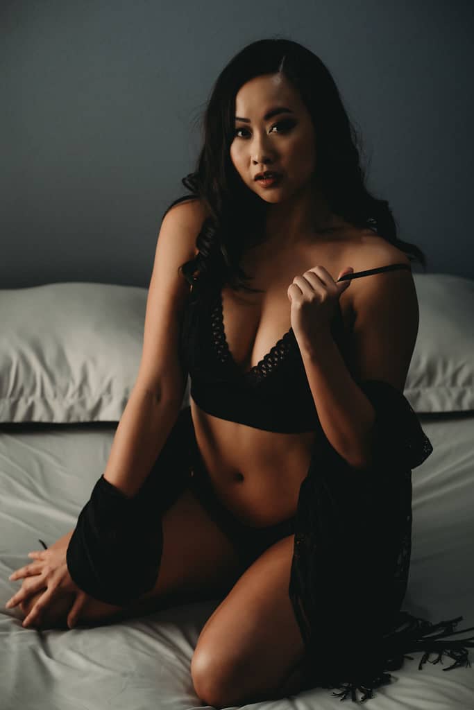 Woman sitting seductively on bed, looking at camera, holding her bra strap wearing matching black underwear and a black cardigan over her arms. Photo by Embodied Art Boudoir. Intentions, intention setting, goal setting, boudoir photoshoot, boudior, buodoir, Denver boudoir, Colorado boudoir, boudoir photographer, self love, growth journey, affirmations, positive intentions, positive affirmations, self love journey, boudoir photography, Denver portrait photography, Denver portrait photographer, Boulder boudoir, fort collins boudoir, colorado springs boudoir, how to set an intention
