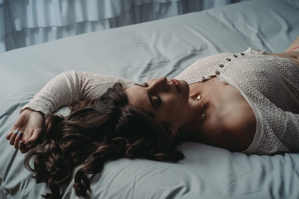 Woman wearing crop top laying on the bed with open hair & closed eyes. Photo by Embodied Art Boudoir. Self care, self love, self care ideas, pampering, fast self care, practical self care, breathwork, save time, mantra, yoga, meditate, busy days, lower stress, boundaries, denver boudoir, photographer