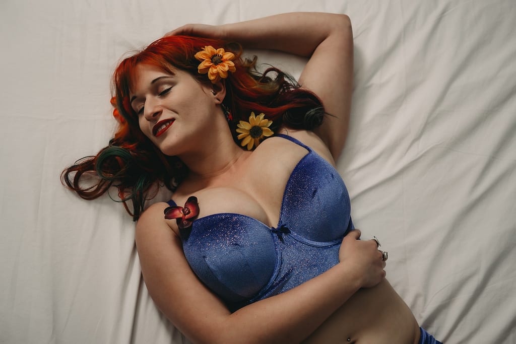 Red Hair Woman wearing blue lingerie with flowers on the top lying on the white bed, Photo by Embodied Art Boudoir.  What not to do, Boudoir photography, colorado boudoir, denver boudoir, boulder boudoir, colorado springs boudoir, boudoir ideas, boudoir poses, boudoir inspiration, boudoir outfits, curvy boudoir, plus size lingerie, lingerie, photoshoot outfits, flattering outfits, curvy lingerie, lingerie look, lingerielook photoshoot, lingerie outfit, lingerie outfit bedroom, lingerie party