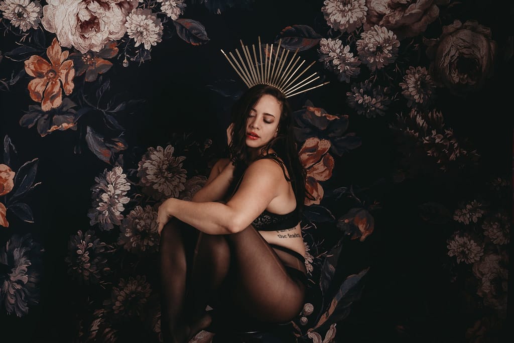 Women wearing black lingerie and golden crown posing in dark room with flower wallpapers in background. Photo by Embodied Art Boudoir. Invest in yourself, investment, self love, self care, body appreciation, growth, growth mindset, learning, massage, rest, volunteer, forgiveness, nvc, nonviolent communication, declutter, self care tips