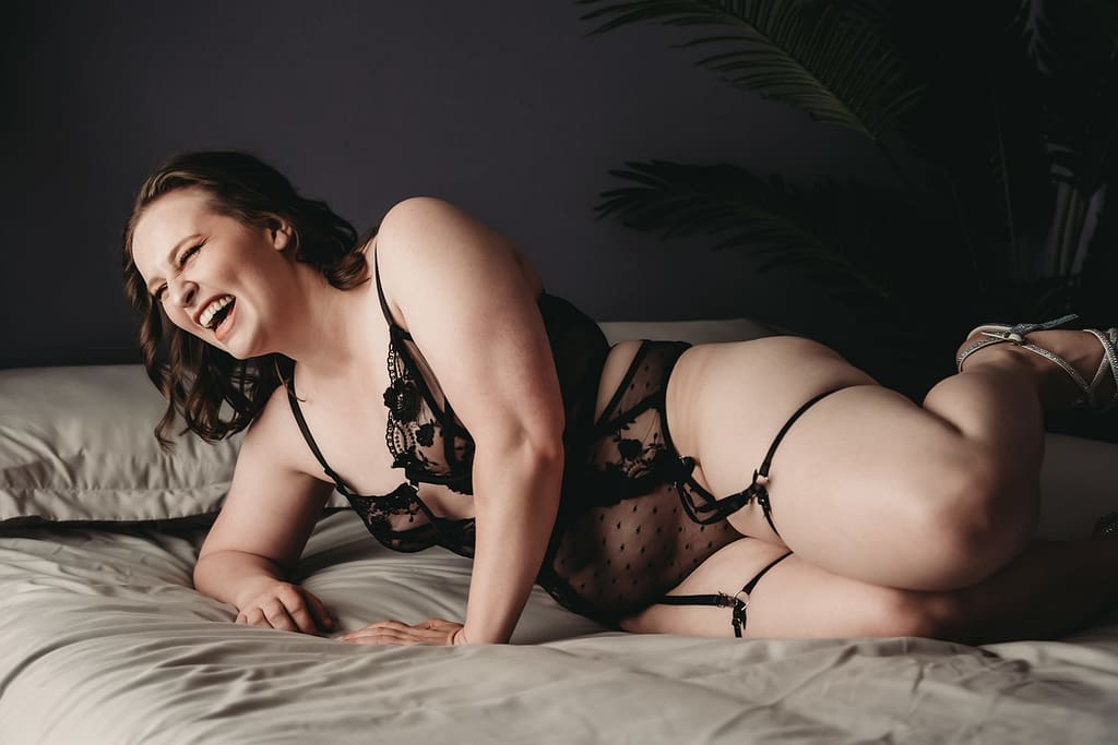 Woman lying on her side, laughing joyfully wearing a black lingere set and high heels. Photo by Embodied Art Boudoir. Deserving, female empowerment, selfcare, self care, me time, enjoy life, something special, Feminine photography, colorado boudoir, denver boudoir, boulder boudoir, colorado springs boudoir, boudoir ideas, boudoir poses, boudoir inspiration, photography inspiration, boudoir session, boudoir photos, boudoir