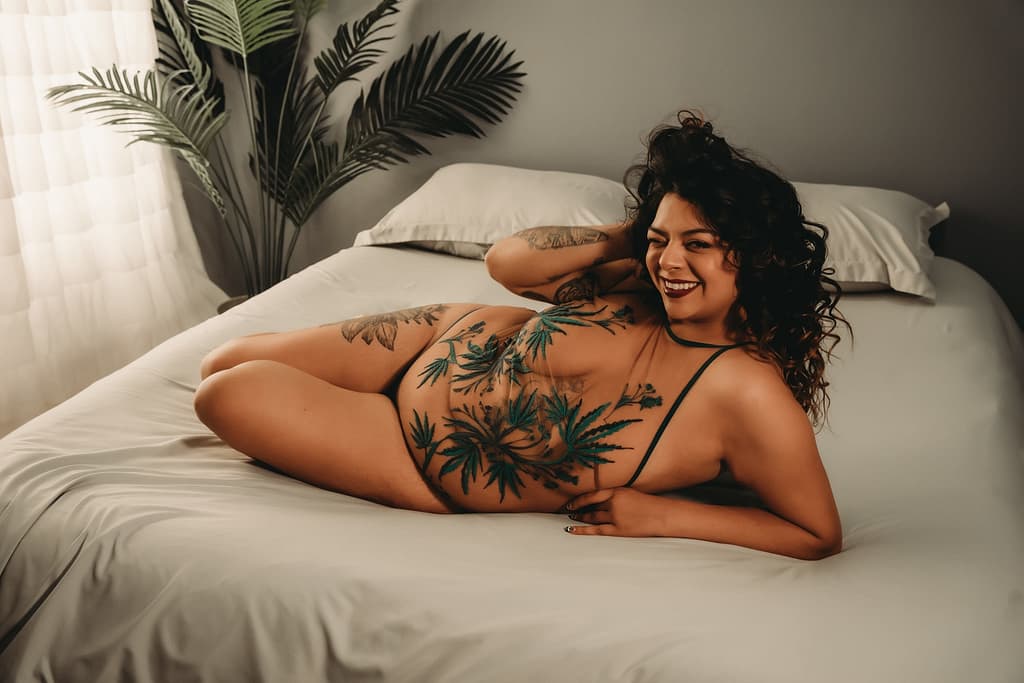 Woman with curly hair lies on her side on bed, wearing a sheer body suit with green embroidery. Photo by Embodied Art Boudoir. Boudoir outfits, boudoir lingerie, boudoir fashion, boudoir babes, boudoir inspo, boudoir fashion, boudoir dress, boudoir style, personal style, favorite outfits, blogging, boudoir ideas, lingerie, colorado boudoir, boudoir, denver boudoir, denver boudior, boulder boudoir, colorado springs boudoir, boudoir ideas, photoshoot accessories, outfit inspiration, photoshoot outfit