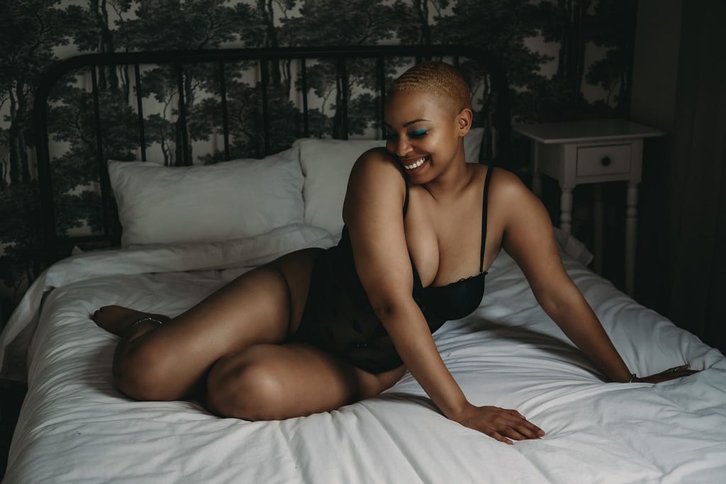 Woman in a black bodysuit laying gracefully on a white bed while smiling shyly, Photo by Embodied Art Boudoir, Colorado boudoir photography, boudoir photo session, boudoir photoshoot, lingerie, happy women, confident women, art photography, body as art, boudoir, portrait, boudoir poses, empowerment through photography, natural hairstyles, empowering photography, professional hair and makeup, self love photoshoot, body positive, self care, luxury photoshoot, confidence, first boudoir photoshoot, Self-Care Ideas for Your Love Language