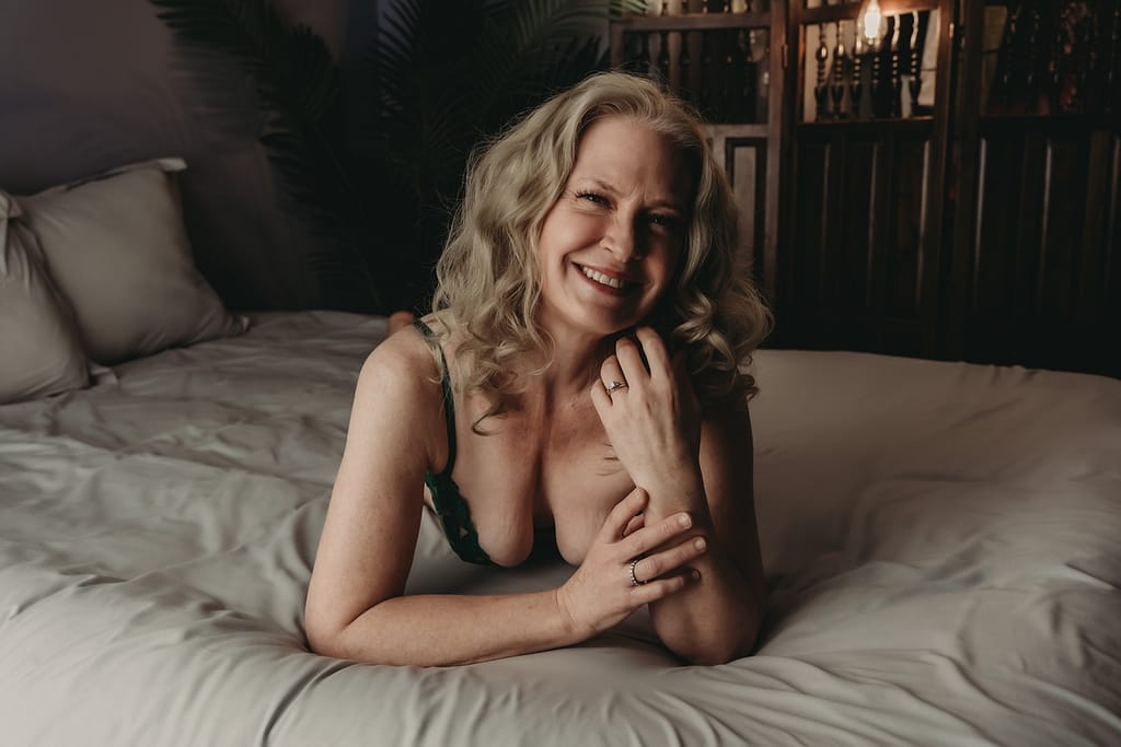 Woman lying on bed smiling brightly at camera, wearing a green bra. Photo by Embodied Art Boudoir. Mindful, mindfulness, brain and body, brain body connection, yoga, pause, live in the moment,  intention, journal, self expression, confidence, express yourself, embodied, boudoir photos,  colorado boudoir, denver boudoir, boulder boudoir, colorado springs boudoir