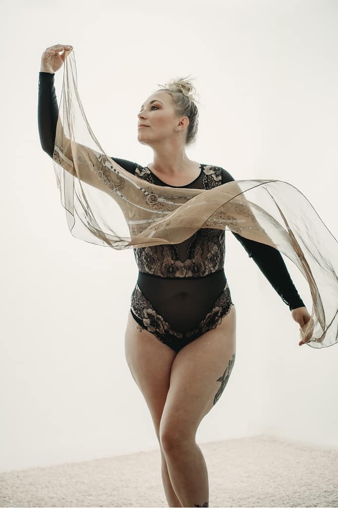 Woman standing in a dance pose, wearing a black body suit and holding a white scarfhoto by Embodied Art Boudoir. Accessories, boudoir outfits, boudoir style, boudoir looks, accessorise, sheets, jewellery, scarf, sheet, creative outfits, sexy look, confidence, boudoir photoshoot, classy photography, sensual photography, sensual boudoir, colorado boudoir, denver boudoir, boulder boudoir, colorado springs boudoir, boudoir ideas 
