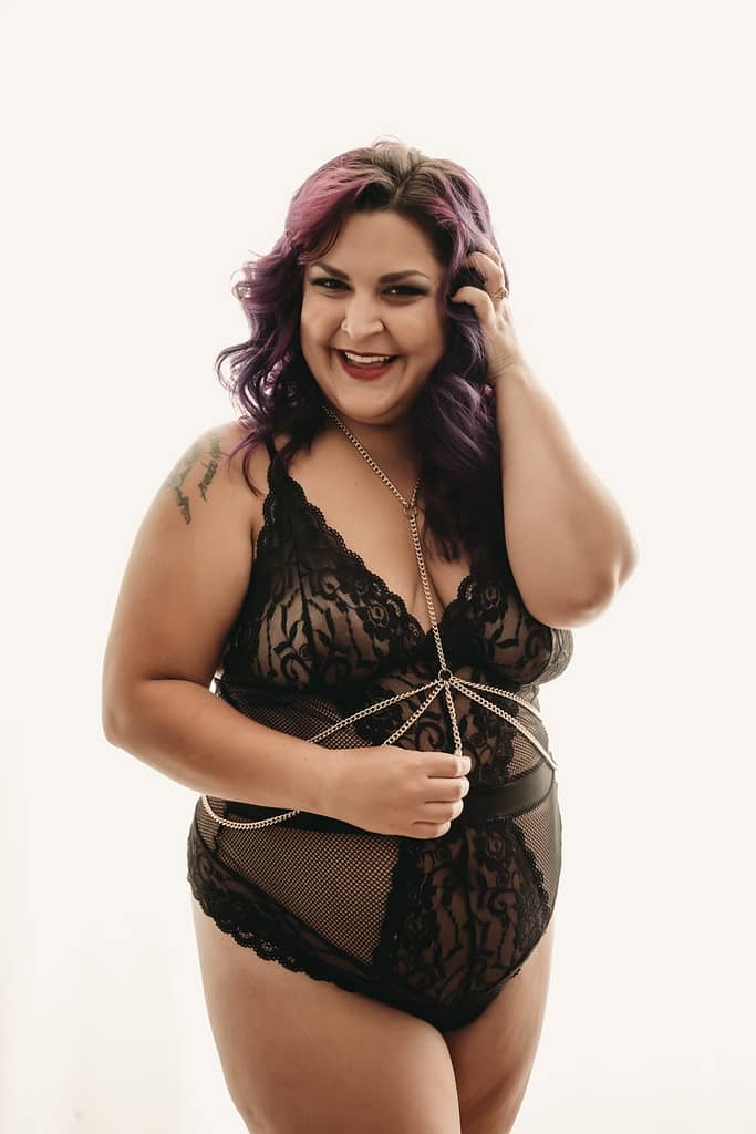 Woman standing with purple hair, wearing a black lacy body suit, smiling wide. Photo by Embodied Art Boudoir. Boudoir images, boudoir bonus, bonus set, printed photos, shower set, photo album, bedsheet, whips and chains, boudoir inspiration, timeless, collection, confidence, remember forever, good deal, priceless, invest in your self, treat yourself, female photographer, female boudoir photographer, empowering women, colorado boudoir, denver boudoir, boulder boudoir, colorado springs boudoir, boudoir ideas, boudoir poses, boudoir inspiration, photography inspiration