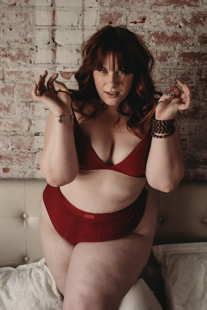 Plus size red haired woman standing confidently looking sultry wearing a matching red bra and briefs. Photo by Embodied Art Studio. Denver boudoir photographer, denver boudoir photography, boudoir, colorado boudoir, denver boudoir, body positive, body positivity, body neutrality, body neutral, fat positive, plus size, petite, body image, body love, self love, self compassion, mirror work, boudoir photos, sexy photos, mindset, beautiful bodies, healing body image