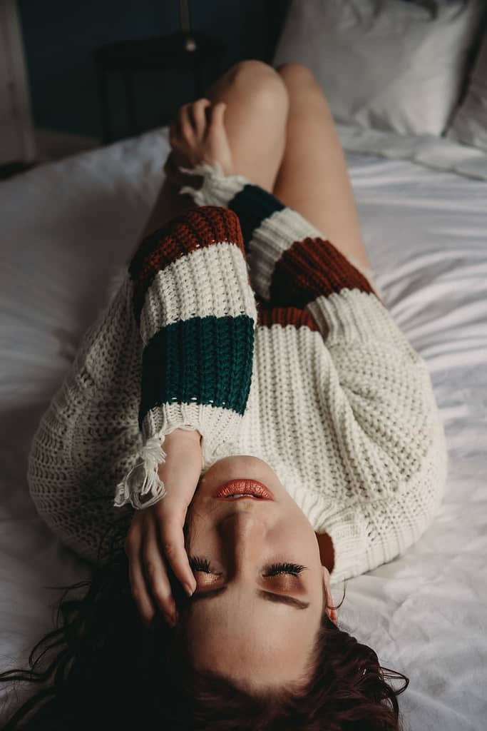 Woman lying on bed with eyes closed wearing a white and striped sweater, with hand resting gently on her face. Photo by Embodied Art Boudoir. Modest boudoir photography, Modest Fashion, Modest Woman, Fashion Trends, Shy, classy photography, classic boudoir, classy boudoir, feminine photography, colorado boudoir, denver boudoir, boulder boudoir, colorado springs boudoir, boudoir ideas, boudoir poses, boudoir inspiration, photography inspiration, boudoir session, boudoir photos
