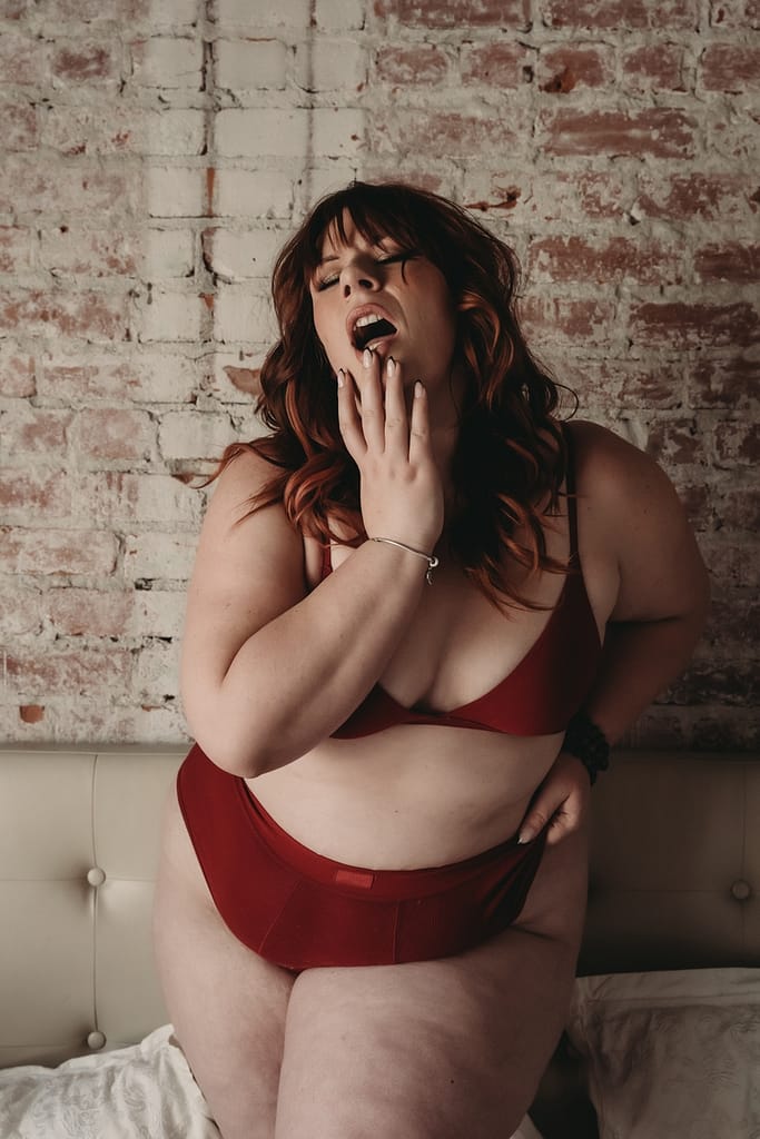 Woman standing next to brick wall wearing a red bralette and panties. Photo by Embodied Art Boudoir. Sexy, plus size, plus size lingerie, lingerie for all, female empowerment, feel good, body inclusivity, comfortable, look good, lingerie, beautiful bras, plus size panties, shop inclusive, support plus size brands, boudoir lingerie, plus size boudoir. 