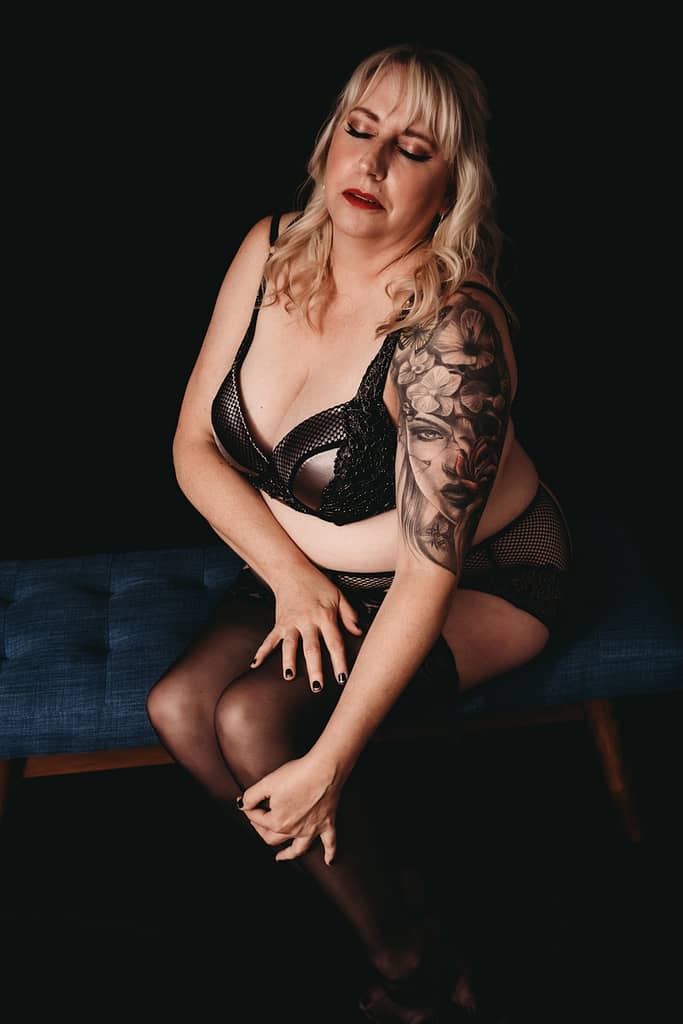 Woman sitting on chair wearing a black bra and panties with stockings. Photo by Embodied Art Boudoir. Sexy, plus size, plus size lingerie, lingerie for all, female empowerment, feel good, body inclusivity, comfortable, look good, lingerie, beautiful bras, plus size panties, shop inclusive, support plus size brands, boudoir lingerie, plus size boudoir. 