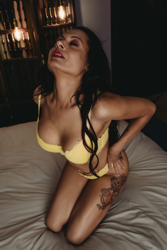 Woman sitting on edge of bed wearing a bright yellow bra, her eyes closed. Photo by Embodied Art Boudoir. Lingerie, Lingerie guide, lingerie types, lingerie terminology, different types of lingerie, what to wear, bra, teddy, body suit, panties, thong, stockings, garters, lingerie inspo, lingerie shopping, female lingerie, female intimates, what to wear, sexy, confidence, stylish, sensual boudoir, colorado boudoir, denver boudoir, boulder boudoir, colorado springs boudoir
